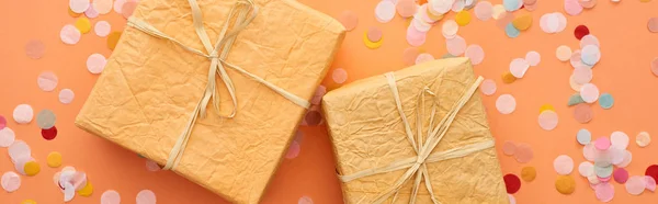 Panoramic shot of gift boxes with bows near confetti on orange — Stock Photo