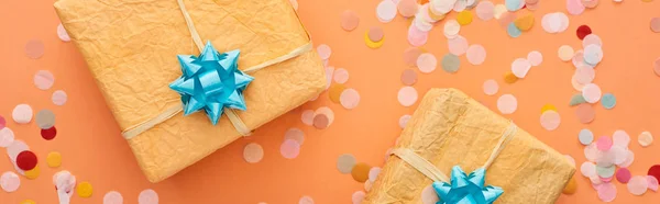 Panoramic shot of blue bows on gift boxes near confetti on orange — Stock Photo