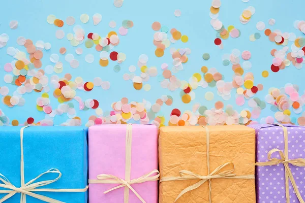 Top view of colorful and wrapped gift boxes near confetti on blue — Stock Photo