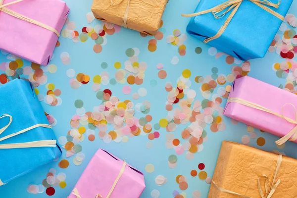 Top view of colorful wrapped gifts near confetti on blue — Stock Photo