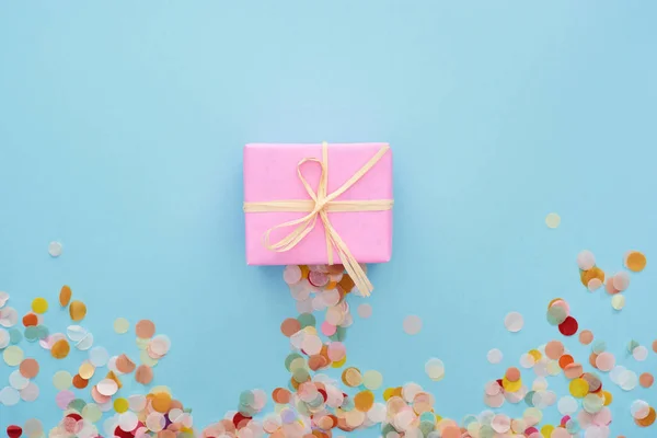 Vue de dessus du présent rose avec arc près de confettis colorés sur bleu — Photo de stock