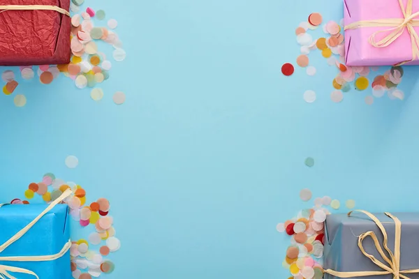 Top view of wrapped presents near colorful confetti on blue — Stock Photo