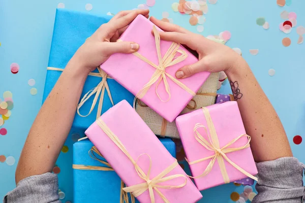 Vista recortada de la mujer agarrando regalos cerca de regalos de colores cerca de confeti en azul - foto de stock