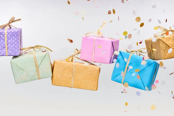 Confettis colorés tombant près de cadeaux enveloppés sur blanc — Photo de stock