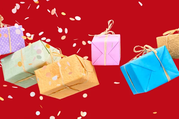 Falling confetti near colorful gift boxes on red — Stock Photo