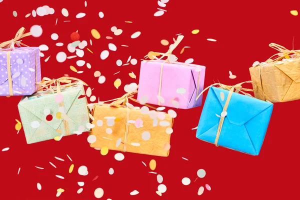 Falling confetti near colorful gifts on red — Stock Photo