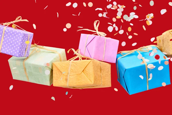 Falling confetti near colorful presents on red — Stock Photo