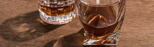Панорамный снимок бренди в стаканах на деревянном столе — стоковое фото