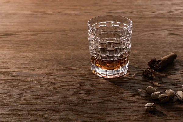 Verre de brandy avec cigare et pistaches sur table en bois — Photo de stock