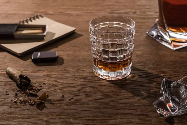 Brandy in vetro e decanter con sigaro, accendino e fiammiferi su tavolo in legno — Foto stock