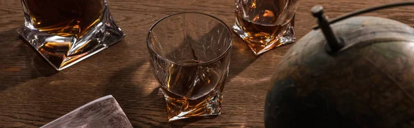 Selective focus of brandy in glasses with globe and map on wooden table, panoramic shot — Stock Photo