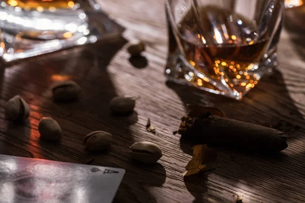 KYIV, UCRANIA - 7 DE NOVIEMBRE DE 2019: Enfoque selectivo de vasos de brandy con naipes, cigarros y pistachos sobre mesa de madera - foto de stock