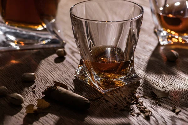 Brandy em copos e decantador com charuto e pistache na mesa de madeira — Fotografia de Stock