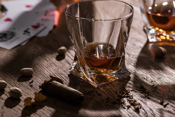 KYIV, UCRANIA - 7 DE NOVIEMBRE DE 2019: Vasos de brandy con cigarro, pistachos y naipes en mesa de madera — Stock Photo