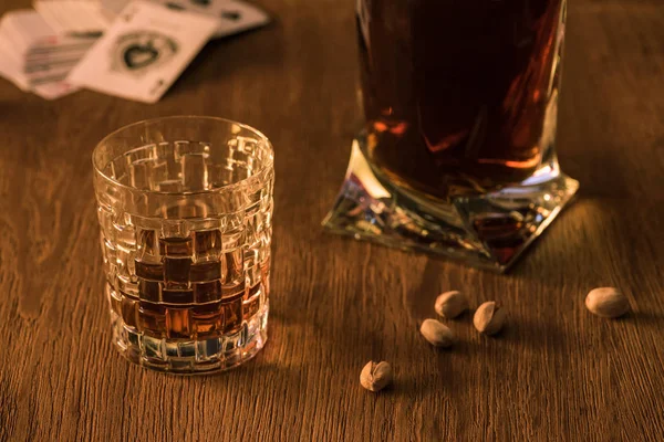 KYIV, UCRAINA - 7 NOVEMBRE 2019: Bicchiere su brandy con decanter, pistacchi e carte da gioco sullo sfondo su tavolo di legno — Foto stock