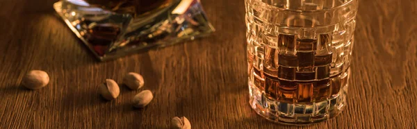 Copa de brandy con pistachos y decantador sobre mesa de madera, plano panorámico - foto de stock