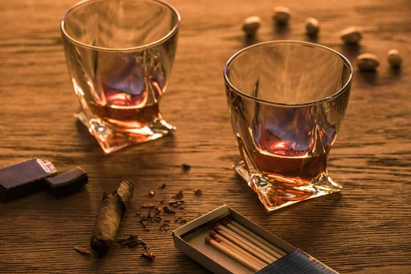 Glasses of brandy with cigar, lighter and pistachios on wooden table — Stock Photo