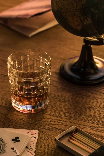 KYIV, UKRAINE - NOVEMBER 7, 2019: Glass of brandy with matches, playing cards and globe on table — Stock Photo