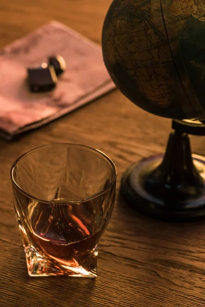 Copo de conhaque com globo e isqueiro no mapa na mesa de madeira — Fotografia de Stock