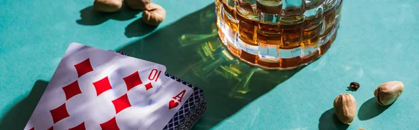 KYIV, UKRAINE - NOVEMBER 7, 2019: Glass of brandy with pistachios and playing cards on green background — Stock Photo