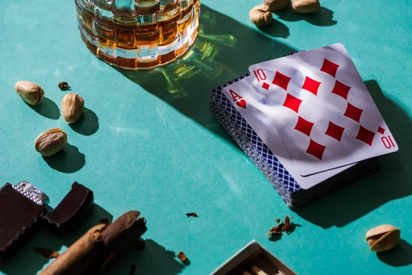 KYIV, UCRANIA - 7 DE NOVIEMBRE DE 2019: Vaso de brandy con pistachos, cartas y cigarros sobre fondo verde - foto de stock