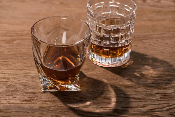 Two glasses of brandy with shadow on wooden table — Stock Photo