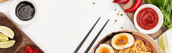 Vue de dessus des ramen épicés près des ingrédients frais et des baguettes sur la surface blanche, vue panoramique — Photo de stock