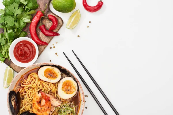Top view of spicy seafood ramen near fresh ingredients and chopsticks on white surface — Stock Photo