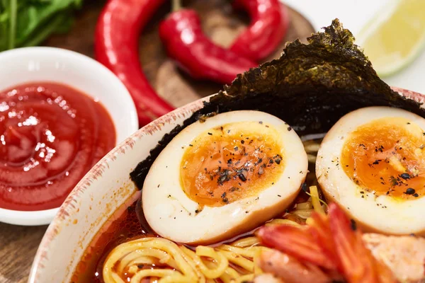 Vista de perto de ramen de frutos do mar picante em tigela com ovo perto de pimenta e molho — Fotografia de Stock