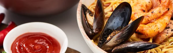 Würzige Meeresfrüchte Ramen in Schüssel auf weißer Oberfläche in der Nähe von Ketchup, Panoramaaufnahme — Stockfoto