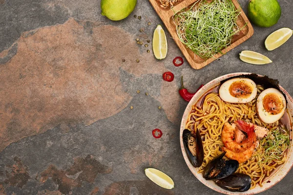 Vista dall'alto del ramen di frutti di mare piccanti vicino a ingredienti freschi sulla superficie di pietra — Foto stock