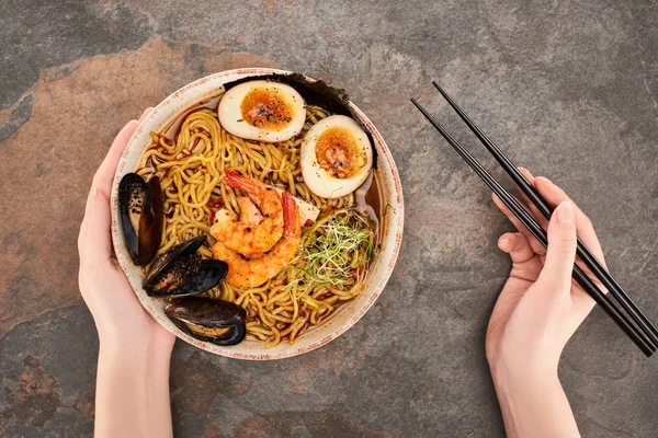 Vista recortada de la mujer comiendo ramen de mariscos picantes con palillos en la superficie de piedra - foto de stock