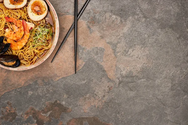 Vue de dessus des ramen épicés de fruits de mer avec des baguettes sur la surface de pierre — Photo de stock