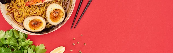 Top view of spicy seafood ramen near chopsticks, parsley and lime isolated on red, panoramic shot — Stock Photo
