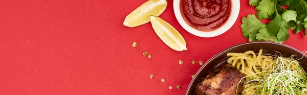 Blick von oben auf würzige Fleisch-Ramen in der Nähe von Sauce, Petersilie und Limette isoliert auf rotem, Panoramaaufnahme — Stockfoto