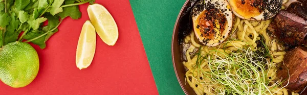 Vista superior de ramen carne picante perto de ingredientes frescos e pauzinhos na superfície verde e vermelha, tiro panorâmico — Fotografia de Stock