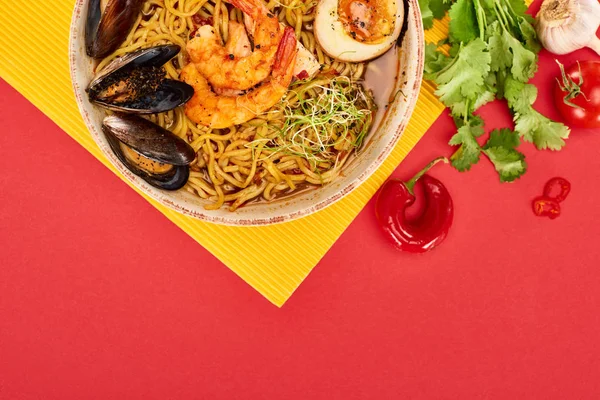 Vue de dessus des ramen épicés de fruits de mer près des ingrédients frais sur la surface jaune et rouge — Photo de stock