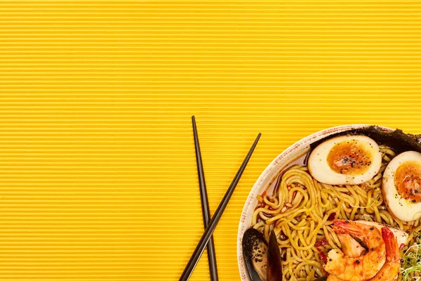 Vue de dessus des ramen de fruits de mer près des baguettes sur la surface jaune — Photo de stock