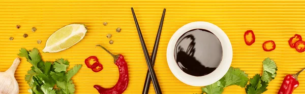 Vue de dessus des épices fraîches, des légumes, de la sauce soja et des baguettes sur surface jaune, vue panoramique — Photo de stock