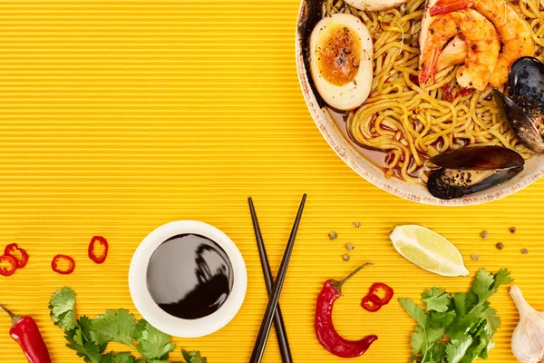 Ansicht von Meeresfrüchten Ramen in der Nähe von frischen Zutaten und Essstäbchen auf gelber Oberfläche — Stockfoto