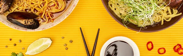 Top view of seafood and meat ramen near fresh ingredients, soy sauce and chopsticks on yellow surface, panoramic shot — Stock Photo