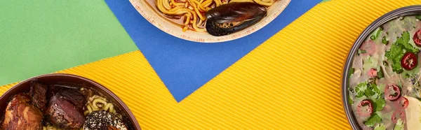 Вид зверху на гострі морепродукти та м'ясний рамен на різнокольоровій поверхні, панорамний знімок — стокове фото