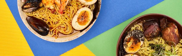 Draufsicht auf würzige Meeresfrüchte und Fleisch-Ramen auf mehrfarbiger Oberfläche, Panoramaaufnahme — Stockfoto