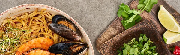 Vista dall'alto di ramen di frutti di mare piccanti vicino a ingredienti freschi sulla superficie grigia, colpo panoramico — Foto stock