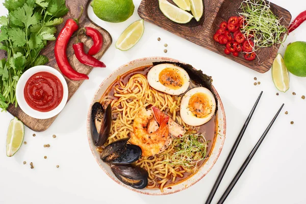 Top view of spicy seafood ramen near fresh ingredients and chopsticks on white surface — Stock Photo