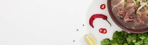 Top view of pho in bowl near chopsticks, lime, chili and soy sauces and coriander on white background, panoramic shot — Stock Photo