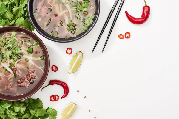 Top view of pho in bowls near chopsticks, lime, chili and coriander on white background — Stock Photo