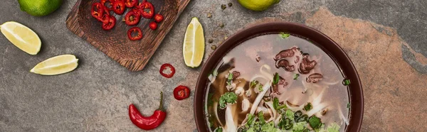 Top view of pho in bowl near lime, chili on stone background, panoramic shot — Stock Photo