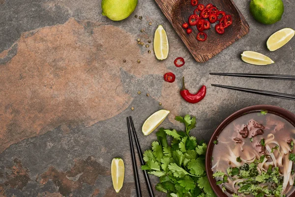 Top view of pho in bowl near chopsticks, lime, chili and coriander on stone background — Stock Photo