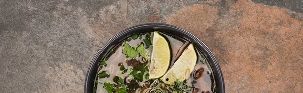 Top view of pho in bowl with lime and coriander on stone background, panoramic shot — Stock Photo